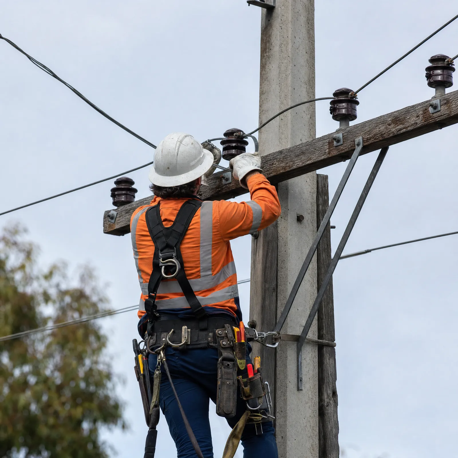 A lineworker in hi-vis and safety harness working on power pole conductors